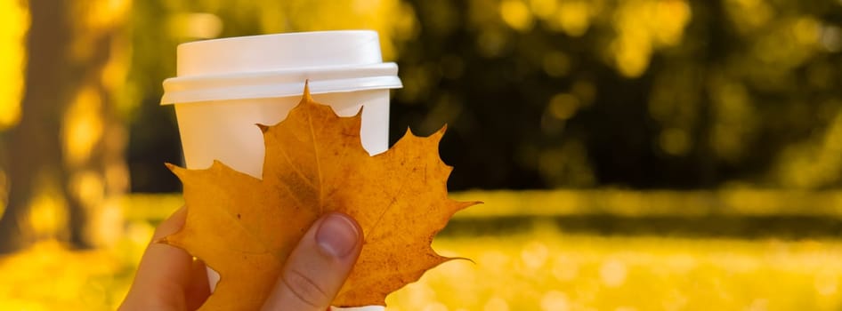 Woman holding Eco zero waste white paper cup copy space mockup Fall autumnal maple yellow leaf next to autumn nature. Cup of tea coffee to go. Hot take away drink cozy mood rest holiday concept. Coffee break lifestyle