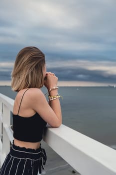 Young woman standing on wooden pier blurred beachside background. Attractive female enjoying the sea shore travel and active lifestyle concept. Springtime. Wellness wellbeing mental health inner peace Slow life digital detox