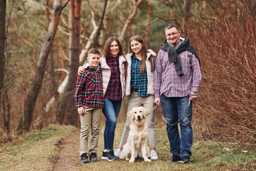 Happy family standing together with their dog outdoors in forest.