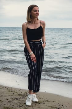 Young woman standing on blurred beachside background. Attractive female enjoying walking the sea shore. travel and active lifestyle concept. Springtime. Relaxation, youth, love, lifestyle solitude with nature. Wellness wellbeing mental health inner peace Slow life digital detox