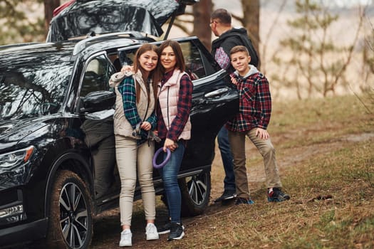 Happy family have fun with their dog near modern car outdoors in forest.