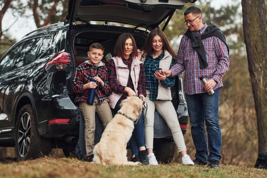 Happy family have fun with their dog near modern car outdoors in forest.