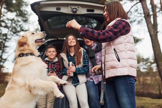 Happy family have fun with their dog near modern car outdoors in forest.