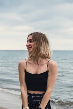 Young woman standing on blurred beachside background. Attractive female enjoying walking the sea shore. travel and active lifestyle concept. Springtime. Relaxation, youth, love, lifestyle solitude with nature. Wellness wellbeing mental health inner peace Slow life digital detox