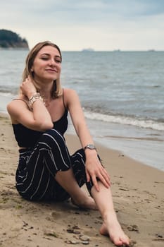 Young woman siting on blurred beachside background. Attractive female enjoying the sea shore. travel and active lifestyle concept. Springtime. Relaxation, youth, love, lifestyle solitude with nature. Wellness wellbeing mental health inner peace Slow life digital detox