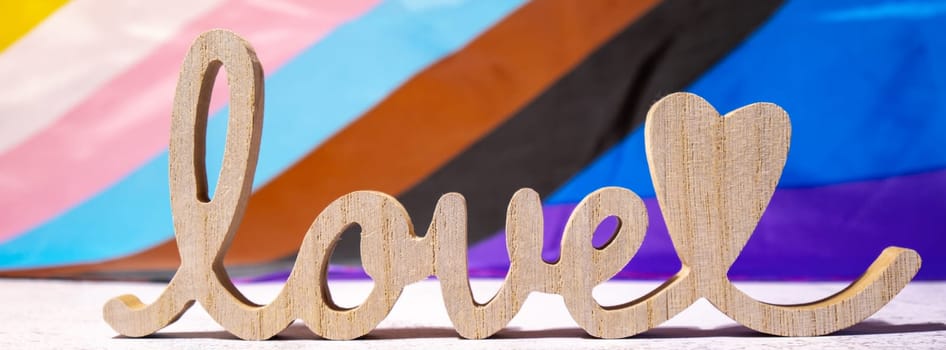 Banner Wooden word love with heart romance on Rainbow LGBTQIA flag made from silk material. Valentine's Day greeting card. Symbol of LGBTQ pride month. Equal rights. Peace and freedom. Support LGBTQIA community. Diversity equality