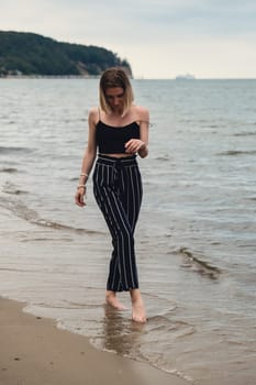 Young woman standing on blurred beachside background. Attractive female enjoying walking the sea shore. travel and active lifestyle concept. Springtime. Relaxation, youth, love, lifestyle solitude with nature. Wellness wellbeing mental health inner peace Slow life digital detox