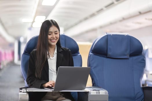 Asian young woman using laptop sitting near windows at first class on airplane during flight, Traveling and Business concept.