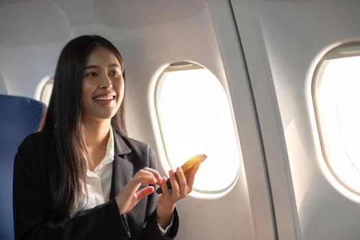 Traveling and technology. Flying at first class. Pretty young business woman using smartphone while sitting in airplane.