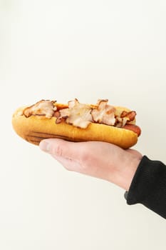 Cropped view of young guy holding tasty hot dog with mustard and ketchup on white background. Street food, delivery