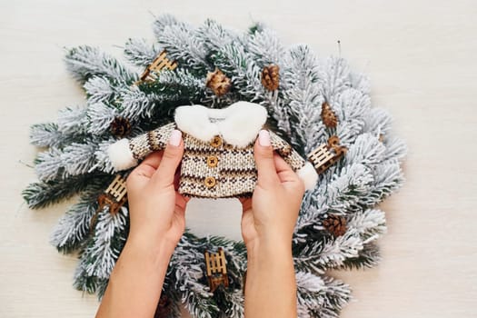 Woman's hands holds little sweater. Top view of christmas festive texture with new year decorations.