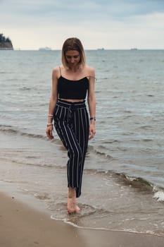 Young woman standing on blurred beachside background. Attractive female enjoying walking the sea shore. travel and active lifestyle concept. Springtime. Relaxation, youth, love, lifestyle solitude with nature. Wellness wellbeing mental health inner peace Slow life digital detox