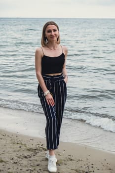 Young woman standing on blurred beachside background. Attractive female enjoying walking the sea shore. travel and active lifestyle concept. Springtime. Relaxation, youth, love, lifestyle solitude with nature. Wellness wellbeing mental health inner peace Slow life digital detox