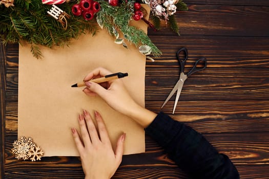 Woman writes on paper. Top view of christmas festive texture with new year decorations.