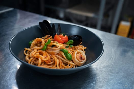 Chef preparing Seafood Pasta with mussels with basil and tomato in black plate