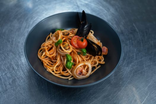 Chef preparing Seafood Pasta with mussels with basil and tomato in black plate