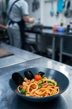 Chef preparing Seafood Pasta with mussels with basil and tomato in black plate