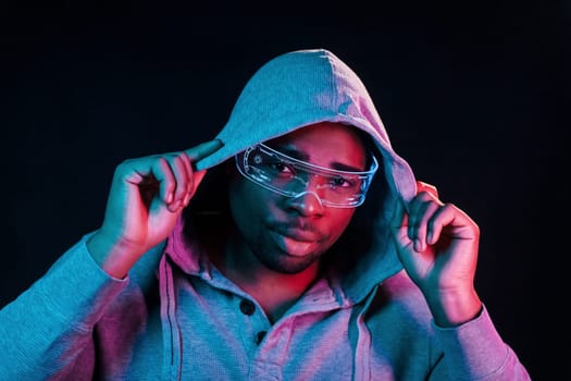 In special eyewear. Futuristic neon lighting. Young african american man in the studio.