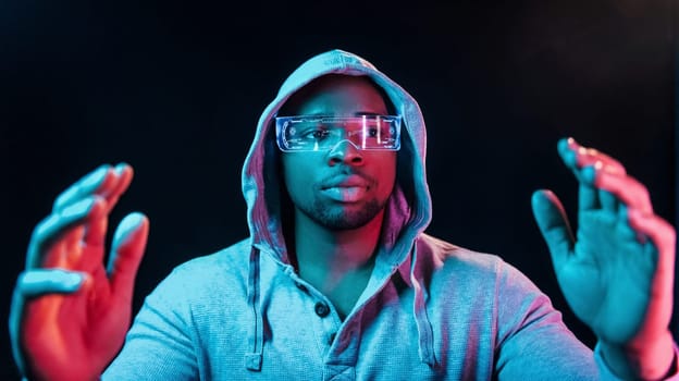 In special eyewear. Futuristic neon lighting. Young african american man in the studio.