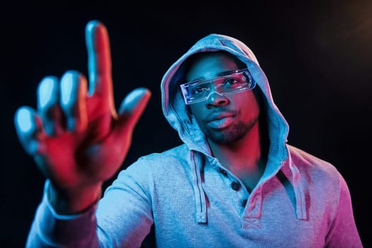 In special eyewear. Futuristic neon lighting. Young african american man in the studio.