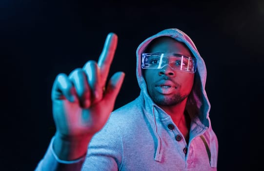 In special eyewear. Futuristic neon lighting. Young african american man in the studio.