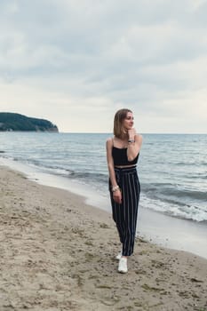 Young woman standing on blurred beachside background. Attractive female enjoying walking the sea shore. travel and active lifestyle concept. Springtime. Relaxation, youth, love, lifestyle solitude with nature. Wellness wellbeing mental health inner peace Slow life digital detox