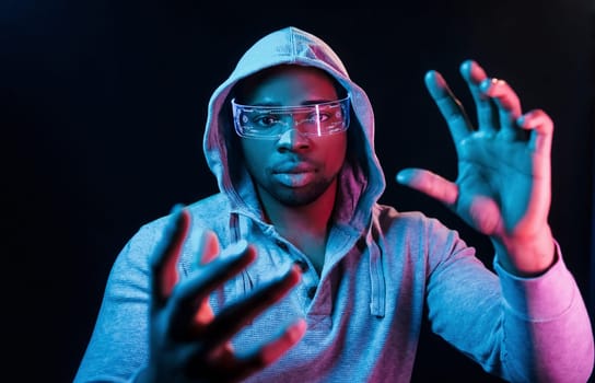 In special eyewear. Futuristic neon lighting. Young african american man in the studio.