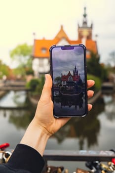 Female traveler in historical places courtyard of landmark and shoots short video on phone. Tourist photographs historic place on sunny day in Gdansk Poland. Unrecognizable woman Tourism and blogging sharing live online for audience travel together recording video on mobile phone