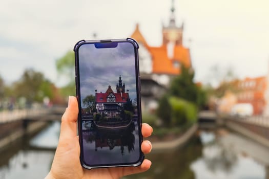 Female traveler in historical places courtyard of landmark and shoots short video on phone. Tourist photographs historic place on sunny day in Gdansk Poland. Unrecognizable woman Tourism and blogging sharing live online for audience travel together recording video on mobile phone