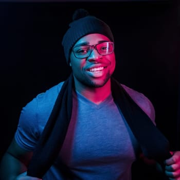 In hat and scarf. Futuristic neon lighting. Young african american man in the studio.