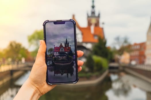 Female traveler in historical places courtyard of landmark and shoots short video on phone. Tourist photographs historic place on sunny day in Gdansk Poland. Unrecognizable woman Tourism and blogging sharing live online for audience travel together recording video on mobile phone