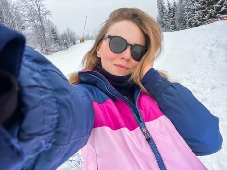 Happy young woman skier taking selfie hiking mountains. Girl smiling Makes Selfie In Ski Clothing On Snow Mountain. Resting relaxing extreme recreation active lifestyle activity technology smart phone mobility internet online concept. Emotions nature on background.