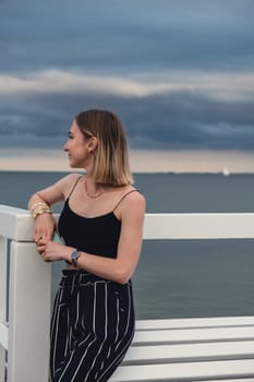 Young woman standing on wooden pier blurred beachside background. Attractive female enjoying the sea shore travel and active lifestyle concept. Springtime. Wellness wellbeing mental health inner peace Slow life digital detox