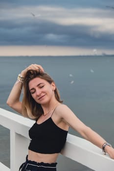 Young woman standing on wooden pier blurred beachside background. Attractive female enjoying the sea shore travel and active lifestyle concept. Springtime. Wellness wellbeing mental health inner peace Slow life digital detox