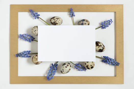 Easter composition with paper blank with text Happy easter, quail eggs, fresh flowers and golden frame.Top view, flat lay.