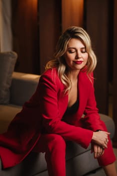 a beautiful girl dressed in a red formal suit posing in a modern interior.