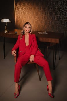 a beautiful girl dressed in a red formal suit posing in a modern interior.