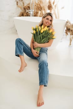 Cute smiling girl with a bouquet of yellow tulips in the interior.