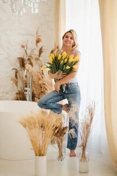 Cute smiling girl with a bouquet of yellow tulips in the interior.