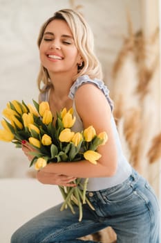 Cute smiling girl with a bouquet of yellow tulips in the interior.