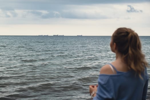 Defocused Young woman standing back on blurred beachside background. Attractive female enjoying walking the sea shore. travel and active lifestyle concept. Springtime. Relaxation, youth, love, lifestyle solitude with nature. Wellness wellbeing mental health inner peace Slow life digital detox