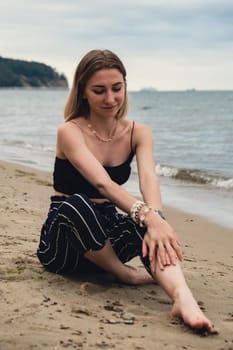 Young woman siting on blurred beachside background. Attractive female enjoying the sea shore. travel and active lifestyle concept. Springtime. Relaxation, youth, love, lifestyle solitude with nature. Wellness wellbeing mental health inner peace Slow life digital detox