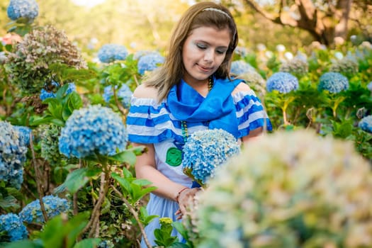 Portrait of girl in traditional Central American folk costume holding flowers in a nursery. Beautiful Nicaraguan woman in national folk costume holding flowers in a nursery