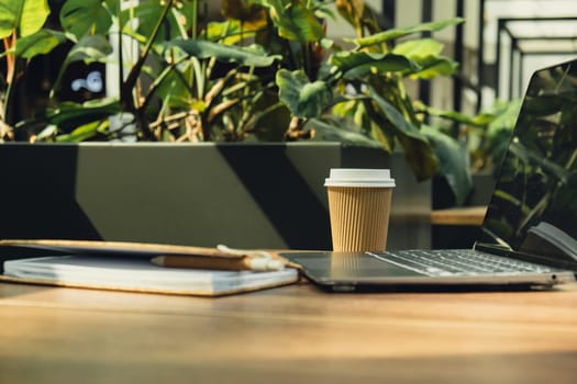 Mock up of modern laptop at table in co-working space. Remote Freelancer's place of work. Study and work online. Remote business education. Concept of webinar. E-learning Workstation Take away recycling coffee from paper cup. Coffee break Technology in Life Copy space