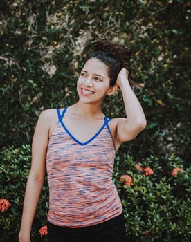 Smiling latin woman near a garden with defocused background, Portrait of smiling woman near a grass wall. Close-up of happy girl near a garden outdoors