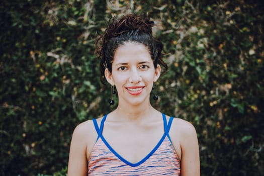 Close-up of happy girl near a garden outdoors. Smiling latin woman near a garden with defocused background, Portrait of smiling woman near a grass wall