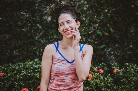 Portrait of smiling woman near a grass wall. Close-up of happy girl near a garden outdoors. Smiling latin woman near a garden with defocused background