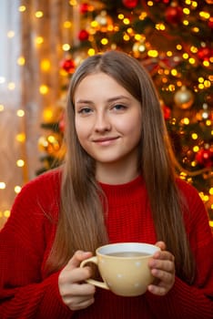 Portrait of a girl with cup of hot tea or coffee with background of Christmas tree