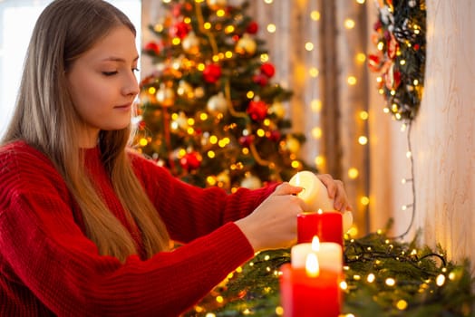 Young blond girl in red sweater igniting candles in decorated living room