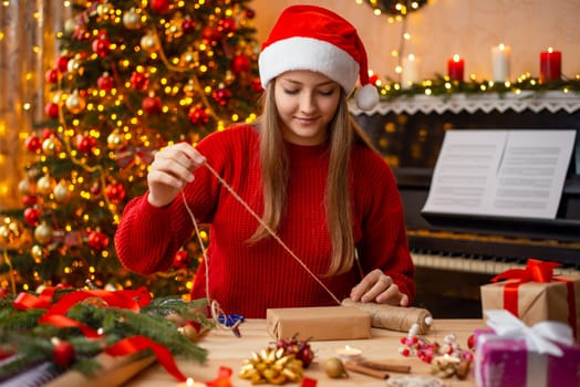 Blond girl in beautifully decorated room with Christmas tree, burning candles preparing presents for close people